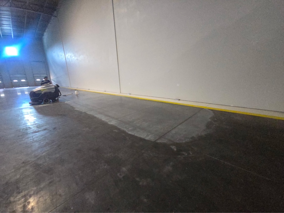 Wide warehouse floor split between dark untreated concrete and the glossy treated section