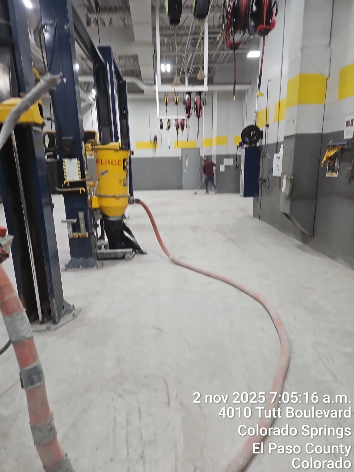 Wide view of an auto shop floor mid-grind in Colorado Springs, dust extraction hose run across the slab