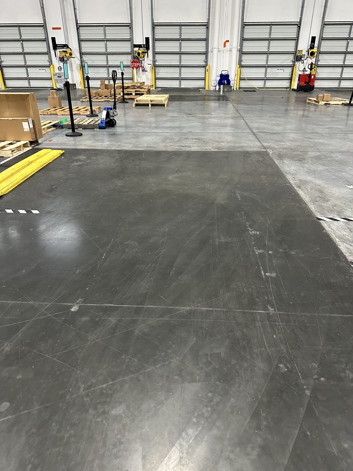 Dark treated dock apron in the foreground meeting untreated gray concrete in front of a row of dock doors