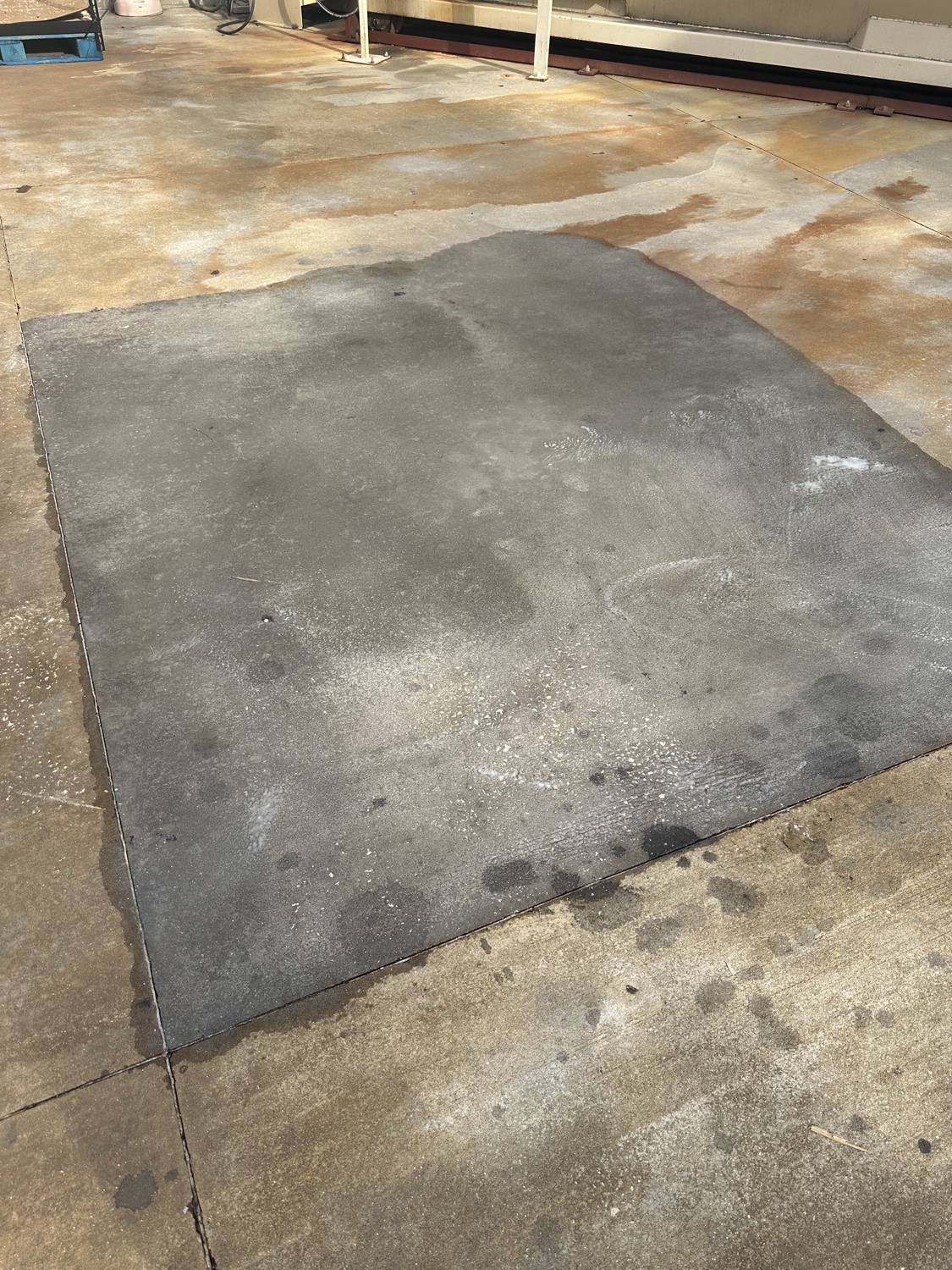 Rust-stained exterior loading pad at a compactor, with a cleaned test patch showing the contrast
