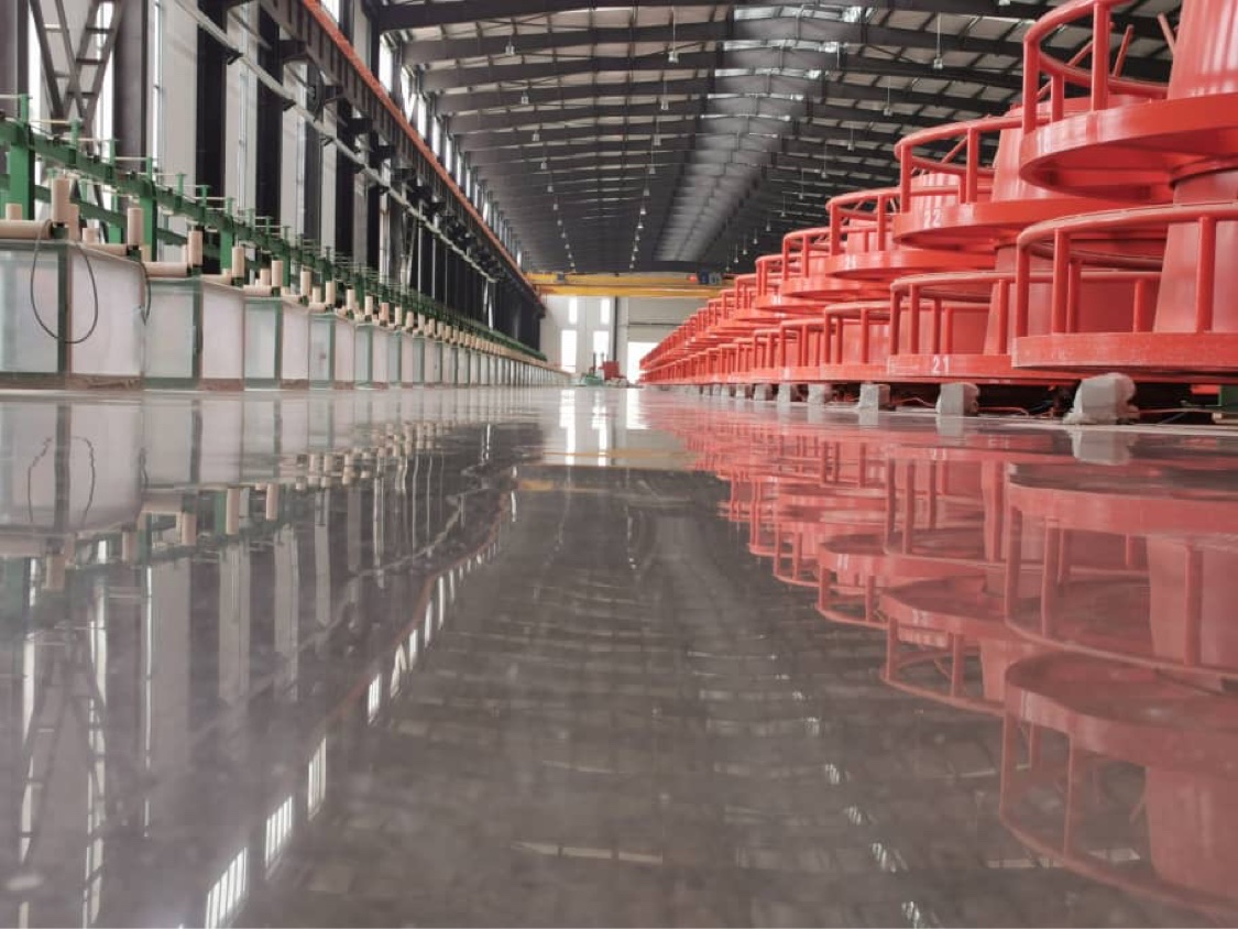 Mirror-finish epoxy plant floor reflecting red industrial machinery and overhead lights