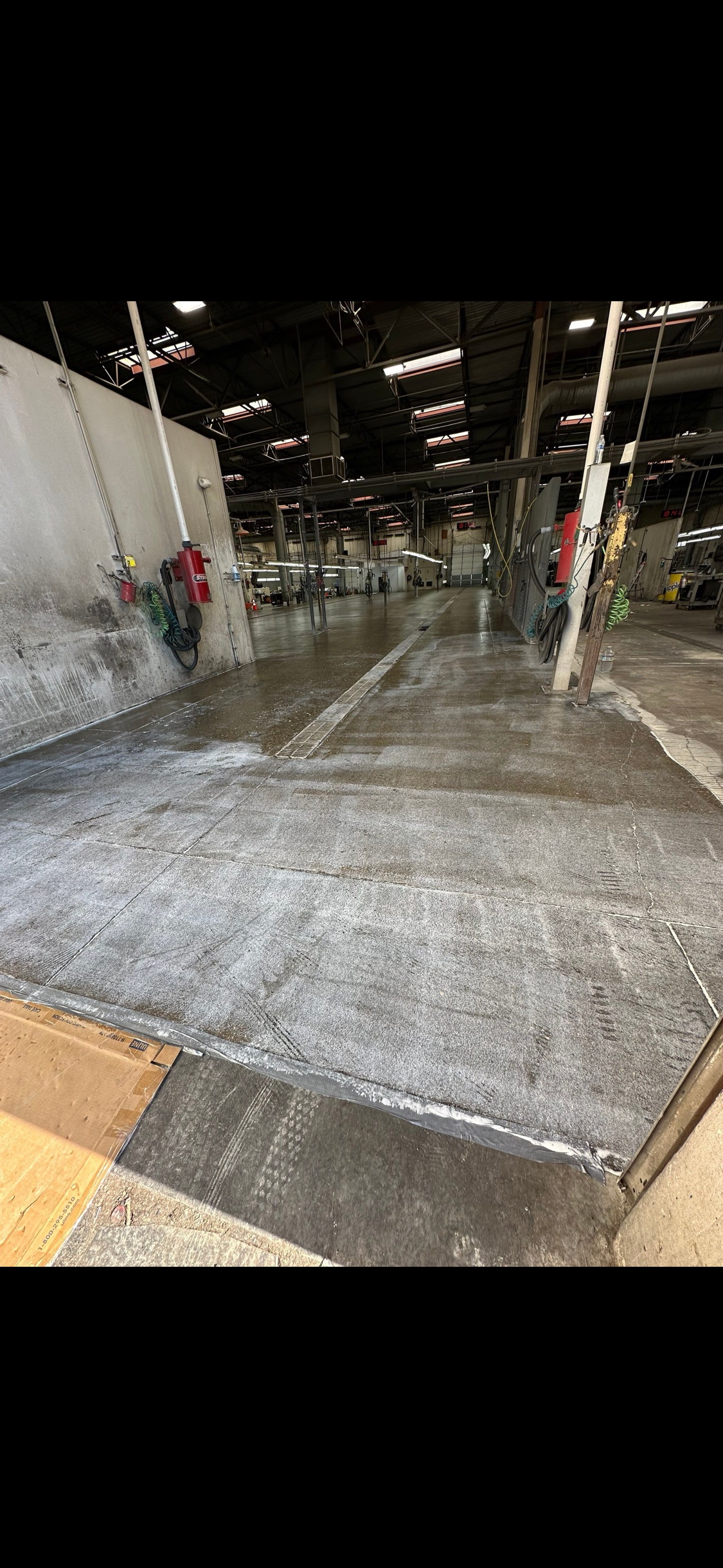 Industrial wash bay floor mid-treatment, prepped surface running down the bay toward the trench drain
