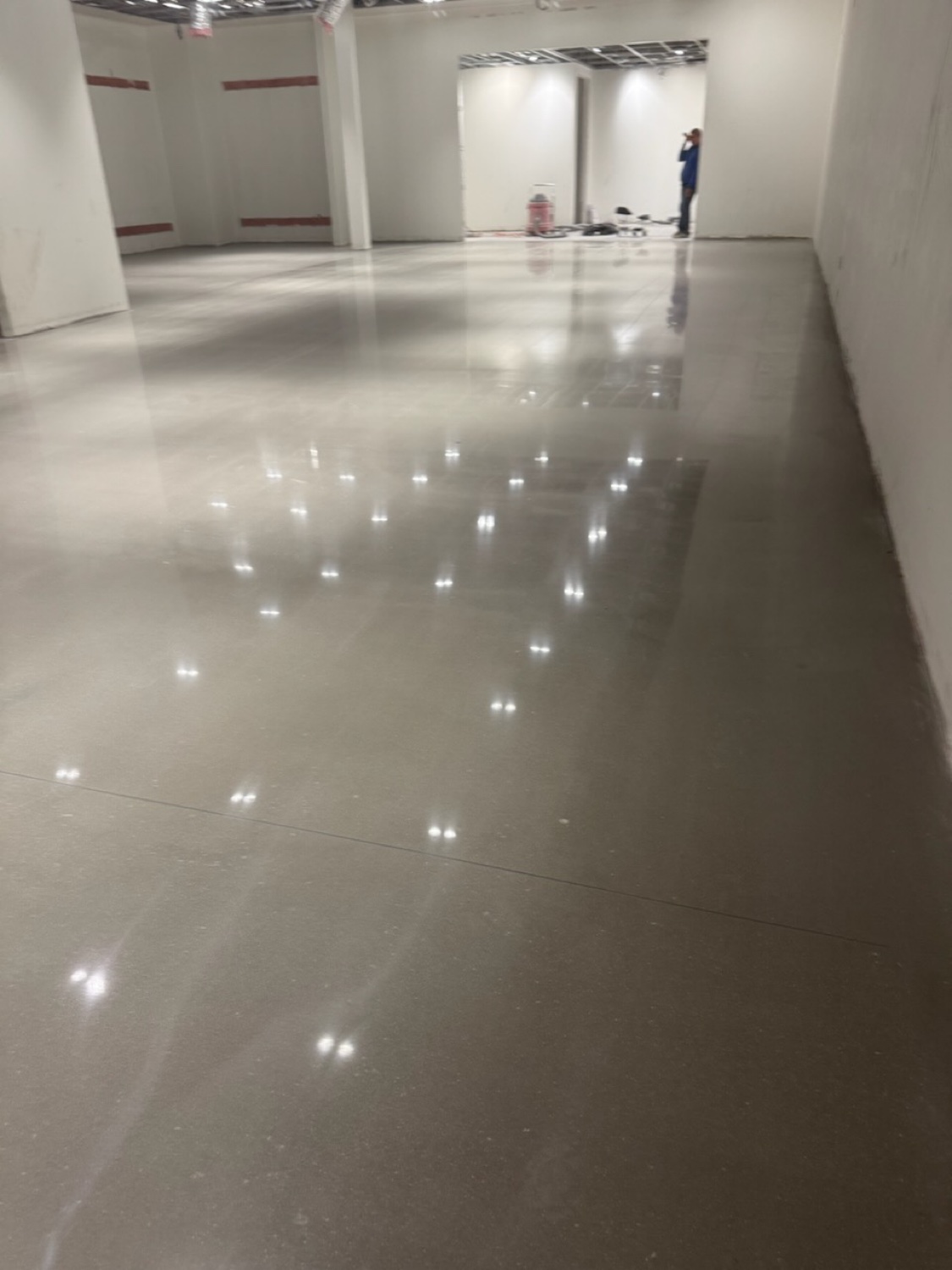 Mirror-polished concrete floor reflecting ceiling lights across an empty retail tenant space