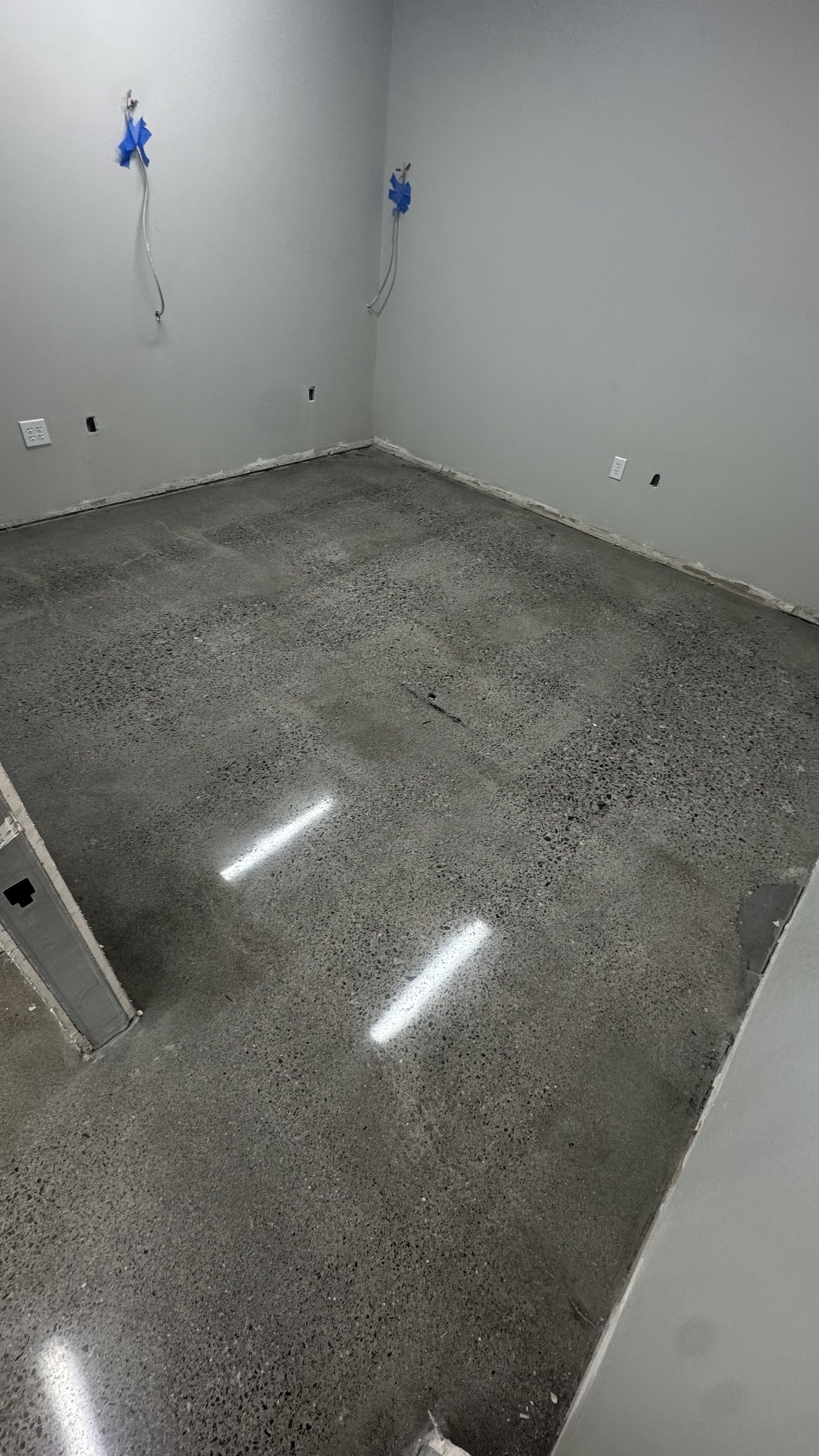 Polished aggregate concrete floor in a small office room, light strips reflecting in the finish