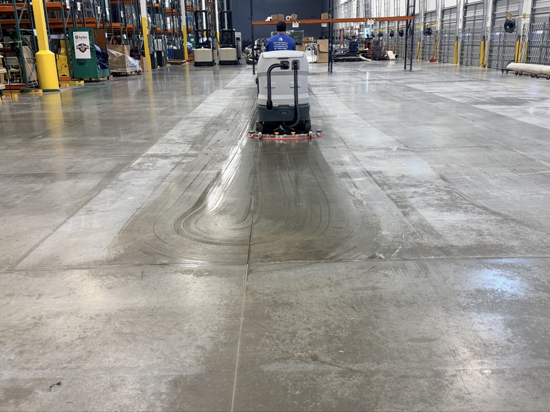 Ride-on scrubber working a warehouse floor while the facility stays in operation around it